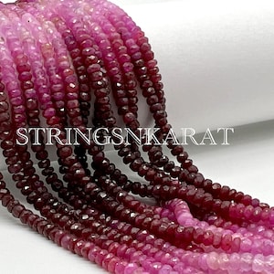 May include: A strand of pink and red ruby beads. The beads are faceted and have a graduated color from light pink to dark red. The beads are strung on a clear thread. The image is labeled "STRINGSNKARAT".