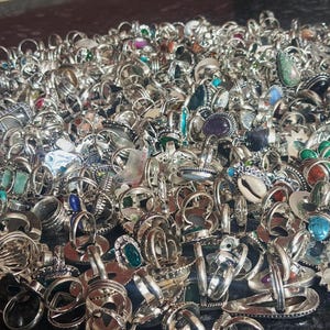 Puede incluir: Una gran colecci&oacute;n de anillos de plata con diversas engastes de piedras preciosas, incluyendo esmeraldas, zafiros y amatistas. Los anillos se muestran en un mont&oacute;n, mostrando una variedad de dise&ntilde;os y tama&ntilde;os. Los anillos est&aacute;n sobre una superficie oscura.