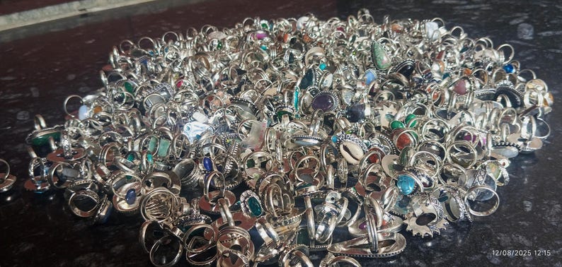 Puede incluir: Una gran colecci&oacute;n de anillos de plata con diversas engastes de piedras preciosas, incluyendo esmeraldas, zafiros y amatistas. Los anillos se muestran en un mont&oacute;n, mostrando una variedad de dise&ntilde;os y tama&ntilde;os. Los anillos est&aacute;n sobre una superficie oscura.