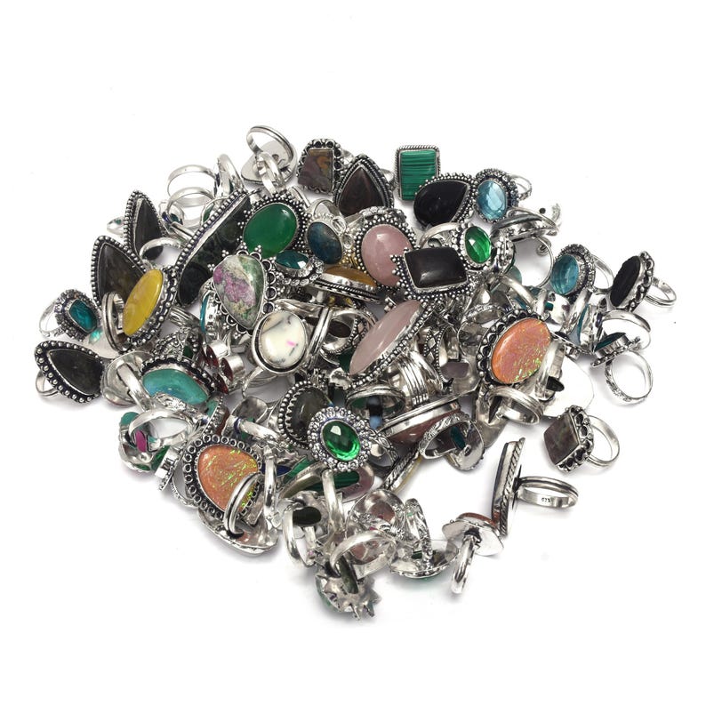 Puede incluir: Un conjunto de anillos de plata con diversas piedras preciosas, incluyendo piedras verdes, rosas y negras. Los anillos tienen diferentes formas y tama&ntilde;os, algunos con dise&ntilde;os intrincados. Las piedras est&aacute;n engastadas en bandas de plata.