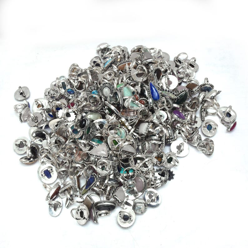 Puede incluir: Un mont&oacute;n de anillos de plata con diversos engastes de piedras preciosas. Los anillos presentan una variedad de piedras de colores, incluyendo azul, verde y morado, sobre un fondo blanco. Los anillos tienen diferentes formas y tama&ntilde;os.