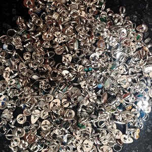 Puede incluir: Una gran colecci&oacute;n de anillos de plata con diversos dise&ntilde;os y piedras preciosas. Los anillos est&aacute;n dispersos, mostrando una variedad de formas, tama&ntilde;os y adornos, incluyendo turquesas, &oacute;palos y otras piedras de colores. La imagen es tomada desde arriba.