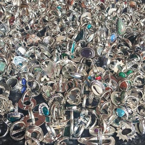 Puede incluir: Una gran colecci&oacute;n de anillos de plata con diversos engastes de piedras preciosas, incluyendo turquesas, amatistas y piedras claras. Los anillos se exhiben en un mont&oacute;n, mostrando una variedad de dise&ntilde;os y tama&ntilde;os. La imagen captura el brillo del metal y los colores de las piedras.