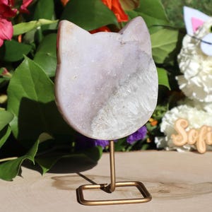 May include: A purple and white agate cat figurine on a gold metal stand. The figurine is carved in the shape of a cat's head.