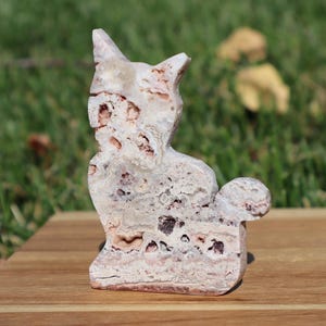 May include: A white and pink agate cat figurine with intricate patterns and swirls. The cat is sitting with its tail curled around its body.