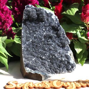 Pode incluir: Uma grande geoda de ametista escura com um exterior áspero e natural. A geoda está cheia de cristais negros brilhantes.