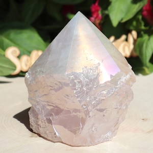 May include: A large, iridescent, clear quartz crystal with a pointed top and a rough, natural base. The crystal has a light pink hue and a rainbow sheen.