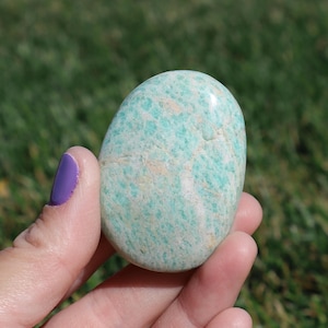 May include: A smooth, green and white, polished amazonite stone. The stone is oval shaped and has a natural, organic look.
