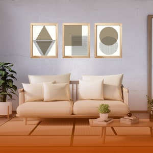 May include: Three framed abstract geometric prints with brown and white stripes and shapes. The prints are hanging on a light gray wall above a light brown couch with white pillows.