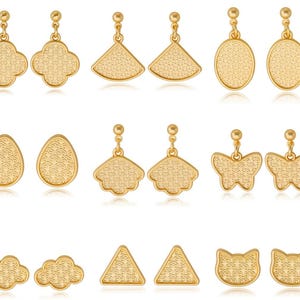 Peut inclure: Une collection de boucles d'oreilles pendantes dorées de différentes formes : trèfles, éventails, ovales, gouttes, papillons, nuages, triangles et visages de chat. Chaque boucle a une surface texturée et une tige pour oreilles percées.