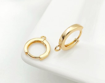 May include: Two gold-colored hoop earrings. The earrings have a smooth, polished finish and a simple, classic design. Each earring has a small loop for attaching to a chain or other jewelry component. The earrings are set against a white background.