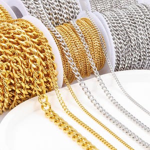 May include: Close-up of three spools of gold and silver chain. The chains are arranged in a row, with the gold chain on the left, the silver chain in the middle, and the gold chain on the right. The chains are all different thicknesses and styles.