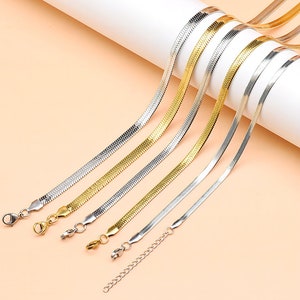 Könnte beinhalten: Ein Set aus sechs silbernen und goldenen Schlangenketten. Die Ketten sind fächerförmig angeordnet, wobei die längste Kette oben und die kürzeste unten liegt. Die Ketten sind alle aus glattem, glänzendem Metall.