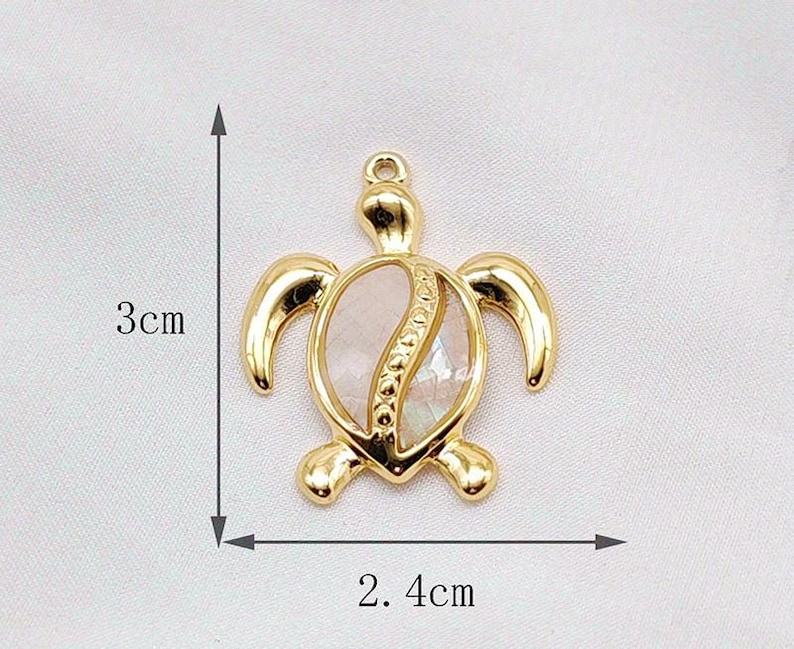 May include: Gold-tone turtle pendant charm with a white shell design. The pendant measures approximately 2.4 inches in length and 3 inches in width.