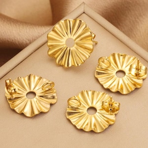 Puede incluir: Cuatro respaldos de pendientes de metal de color dorado con un borde festoneado y un pequeño agujero en el centro.