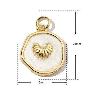 K&ouml;nnte beinhalten: Goldfarbener Anh&auml;nger mit einem wei&szlig;en Emaille-Zentrum, das ein stilisiertes Herzdesign zeigt. Der Anh&auml;nger ist 15 mm breit und 21 mm hoch.