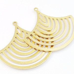 Peut inclure: Deux apprêts de boucles d'oreilles en métal doré avec un motif géométrique. Les apprêts sont en forme de croissant de lune avec une série de cercles concentriques découpés dans le métal.