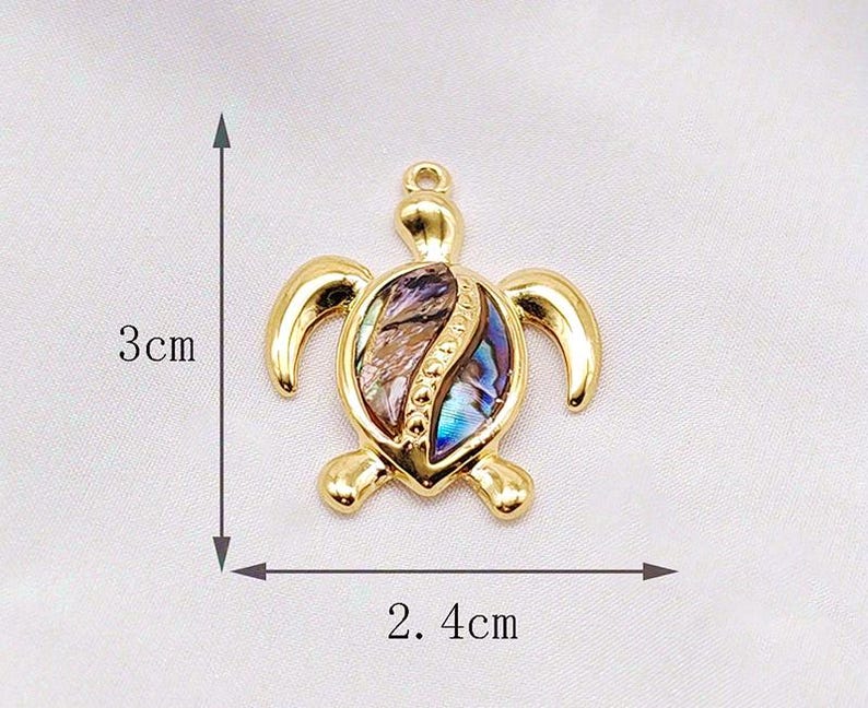 May include: Gold-tone turtle pendant with a shell made of iridescent abalone. The pendant measures 2.4 cm wide and 3 cm tall.