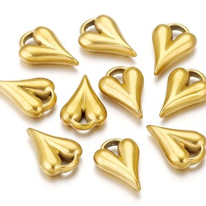 May include: Ten gold-colored heart-shaped charms with a loop at the top. The charms are all the same size and shape, and they are arranged in a circle.
