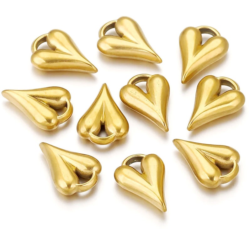 May include: Ten gold-colored heart-shaped charms with a loop at the top. The charms are all the same size and shape, and they are arranged in a circle.