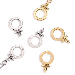 May include: An overhead shot of several metal clasp charms in gold and silver. The charms are in the shape of the Venus symbol, with a circular ring and a cross below. The charms are scattered on a white background.