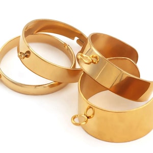 May include: A collection of four gold-coloured metal cuff bracelets with a smooth, polished finish. Each bracelet features a circular loop attachment on the outer edge, designed for connecting additional jewellery components or charms.