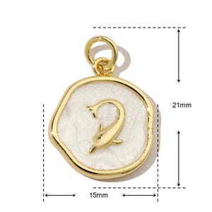 K&ouml;nnte beinhalten: Goldfarbener Anh&auml;nger mit wei&szlig;er Emaille-Oberfl&auml;che. Der Anh&auml;nger zeigt ein stilisiertes Delfin-Design und die Zahl "2" in der Mitte. Der Anh&auml;nger ist 15 mm breit und 21 mm hoch.