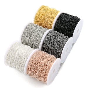 Puede incluir: Cuatro carretes de cadena en diferentes acabados metálicos: oro, plata, negro y oro rosa. La cadena está enrollada alrededor de carretes blancos.
