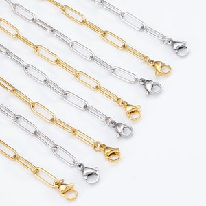 Puede incluir: Varias cadenas de estilo clip de papel en tonos dorados y plateados se muestran sobre un fondo blanco. Cada cadena tiene un cierre de mosquetón. Las cadenas están dispuestas en diagonal, mostrando el contraste entre los eslabones dorados y plateados.