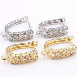 May include: Four earrings: two silver-colored and two gold-colored. Each earring features a rectangular design with a row of small, clear stones. The earrings have a hinged closure and a small loop for attaching charms or other embellishments.