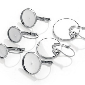 May include: Set of four silver-toned earring blanks with round, clear glass cabochons. The earring blanks have a clip-on closure.