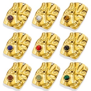 以下が含まれることがあります： 異なる色の宝石のアクセントが付いた、金色の金属製のチャーム9個。各チャームは、テクスチャ加工された抽象的なデザインが特徴です。