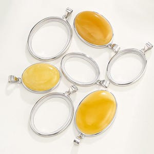 Puede incluir: Seis colgantes ovalados de plata con un bucle de anilla en la parte superior. Cuatro de los colgantes est&aacute;n vac&iacute;os y dos est&aacute;n llenos de piedras de &aacute;mbar amarillo.