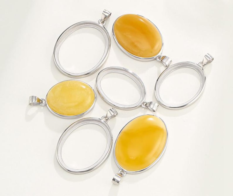 Puede incluir: Seis colgantes ovalados de plata con un bucle de anilla en la parte superior. Cuatro de los colgantes est&aacute;n vac&iacute;os y dos est&aacute;n llenos de piedras de &aacute;mbar amarillo.