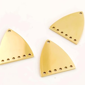 Pode incluir: Três achados de joalheria triangulares de metal dourado. Cada achado tem uma borda inferior arredondada com seis pequenos orifícios e um único orifício na parte superior pontiaguda. Os achados são exibidos em um fundo branco.