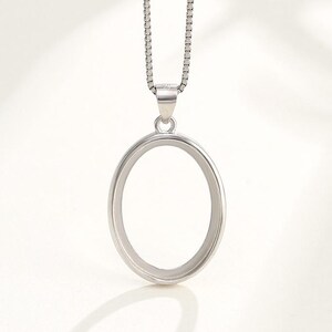 Puede incluir: Un collar con un colgante ovalado de plata y una cadena. El colgante es de forma ovalada simple con una superficie lisa.