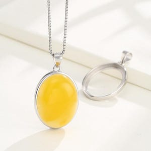 Puede incluir: Un collar de cadena de plata con un colgante que presenta una piedra preciosa ovalada amarilla. El colgante est&aacute; engastado en un marco ovalado de plata.