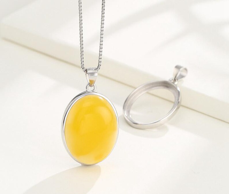 Puede incluir: Un collar de cadena de plata con un colgante que presenta una piedra preciosa ovalada amarilla. El colgante est&aacute; engastado en un marco ovalado de plata.