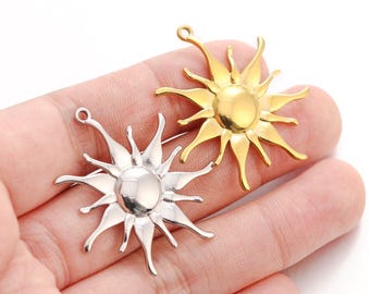 May include: Two metal sun charms, one gold and one silver, with a detailed design of sun rays. The charms are on a hand.