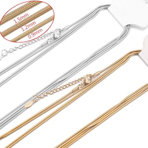 May include: Close-up of three stainless steel snake chains in silver and gold. The image shows the chain thickness: 1.5mm, 1.2mm, and 0.9mm. Each chain has a clasp and an extender chain.