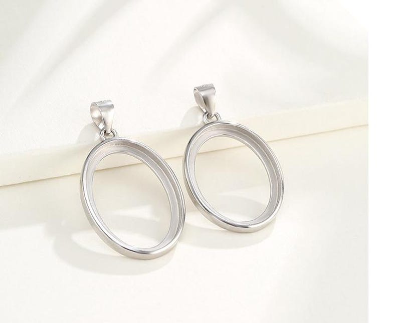 Puede incluir: Dos colgantes ovalados de plata con un acabado liso y pulido. Los colgantes tienen un bucle en la parte superior para sujetar una cadena.