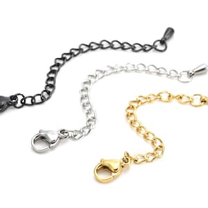 May include: Three metal chain extenders in black, silver, and gold. Each extender has a lobster clasp at one end and a small loop or cone at the other. The chains are made of small, interconnected links.
