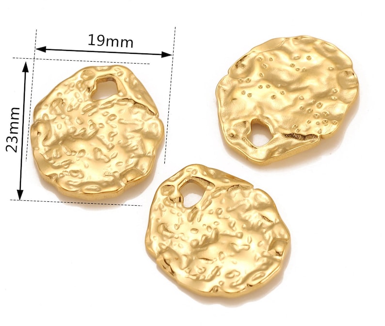 Może przedstawiać: Dwa złote metalowe charms o nieregularnej, fakturowanej powierzchni. Każdy charm ma otw&oacute;r w środku. Charms mają średnicę około 19 mm.