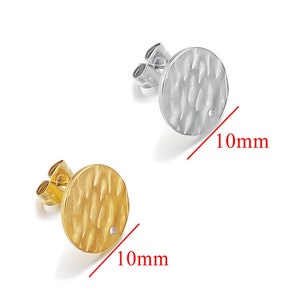 Könnte beinhalten: Zwei runde, strukturierte Ohrringe, einer silber und einer gold, jeweils mit einem kleinen, klaren Stein in der Mitte. Die Ohrringe haben einen Durchmesser von 10 mm.