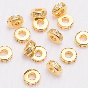 Peut inclure: Un ensemble de 12 perles d'espacement dorées avec des accents de strass clairs. Les perles sont rondes et ont un trou au centre pour le perlage.