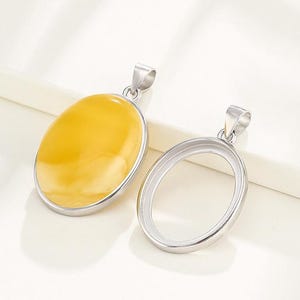 Puede incluir: Un colgante de plata con una piedra ovalada amarilla. El colgante est&aacute; sobre una superficie blanca.