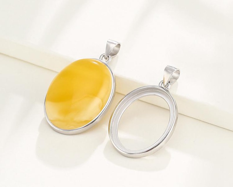Puede incluir: Un colgante de plata con una piedra ovalada amarilla. El colgante est&aacute; sobre una superficie blanca.