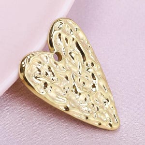 May include: A gold heart-shaped pendant with a textured surface. The pendant has a detailed design with a raised pattern.