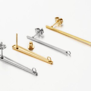 May include: Three pairs of earring findings, two silver and one gold, with a long, straight post and a small loop at the end.