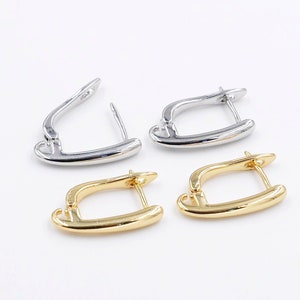 May include: Two pairs of earring findings, one pair is gold and the other is silver. The findings are shaped like a small, open hoop.